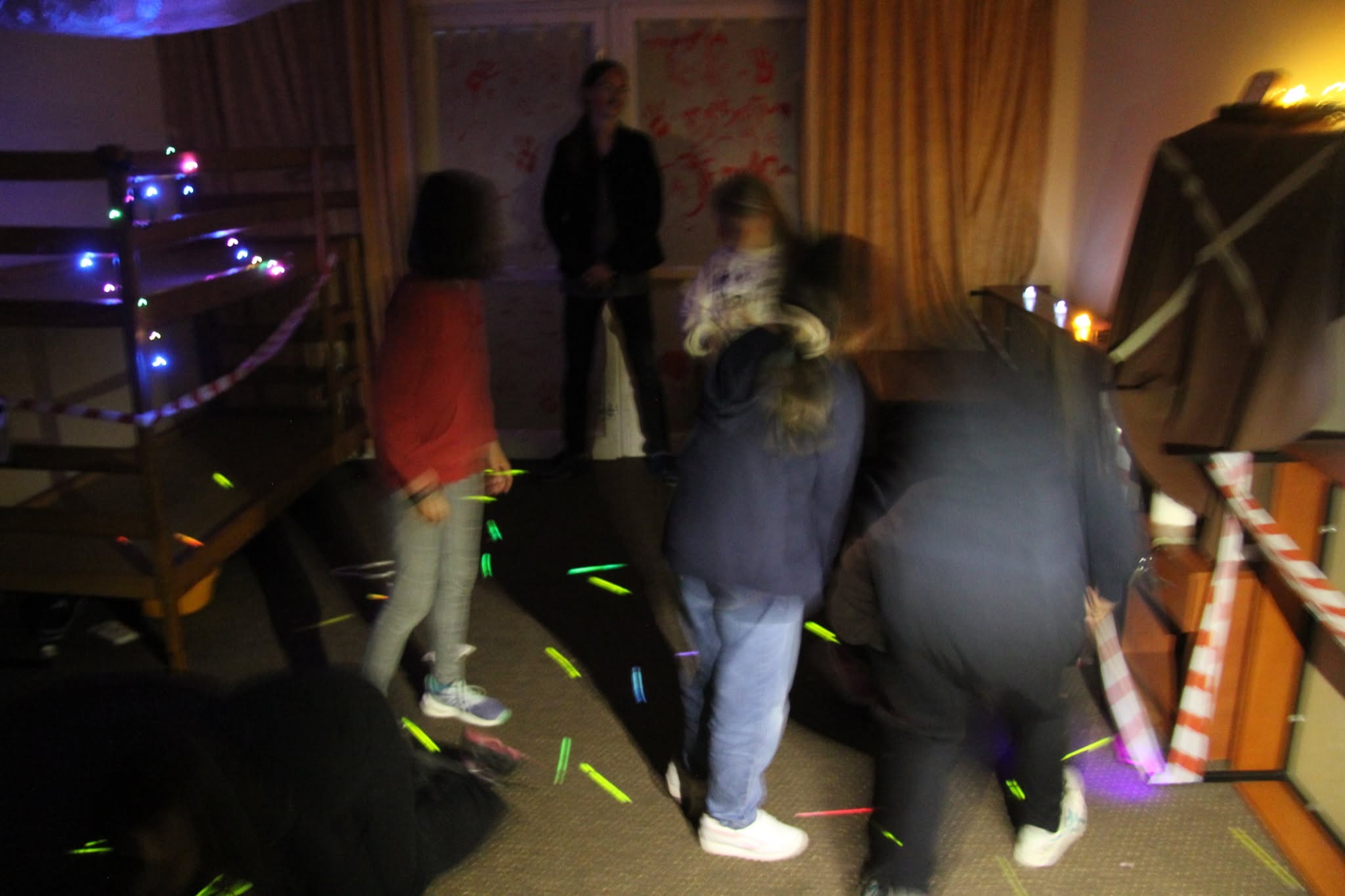 Uczestnicy podczas escape roomu w ciemnym pokoju ze świecącymi pałeczkami
