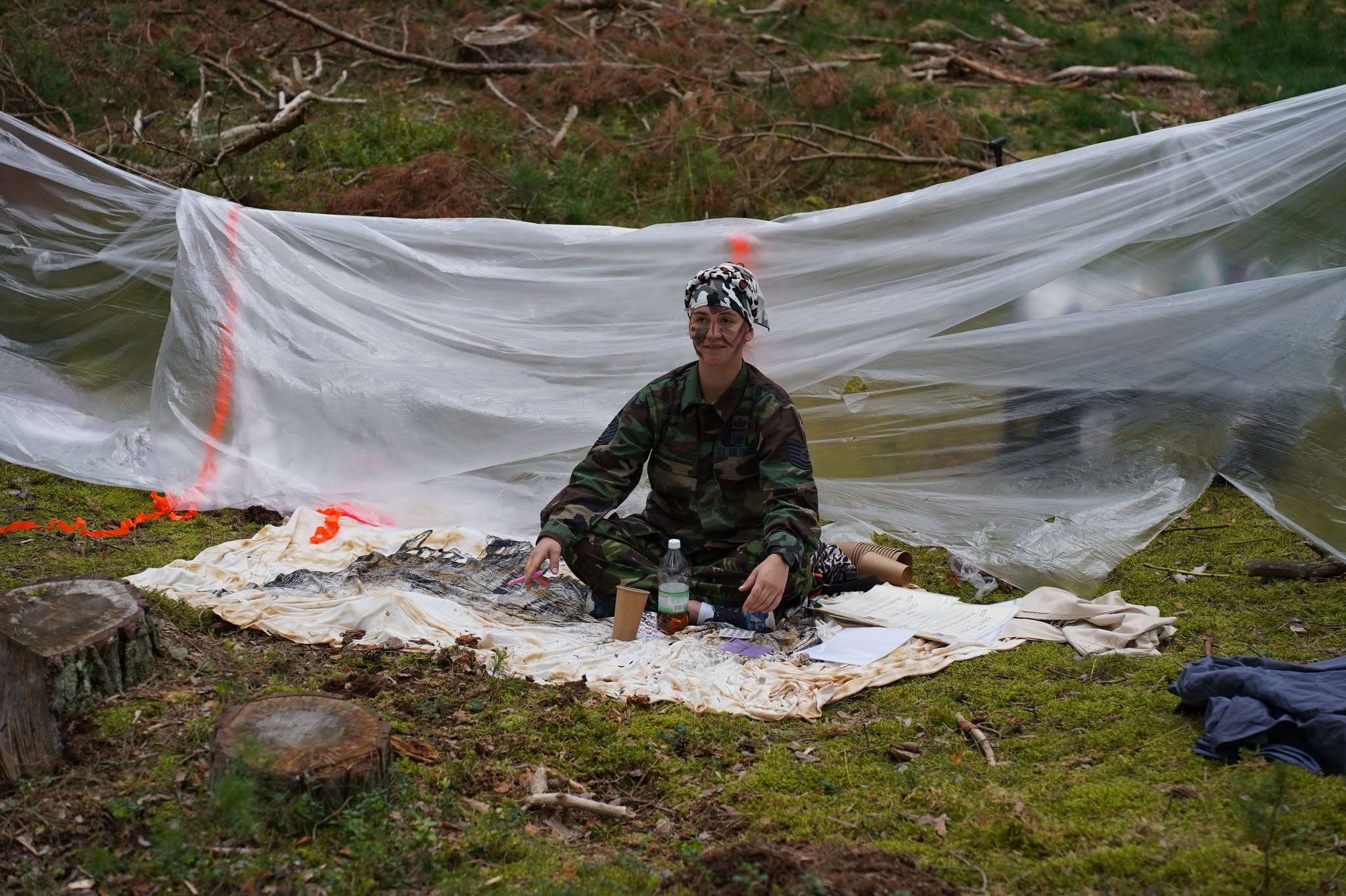 Instruktor w stroju survivalowym przy prowizorycznym schronieniu